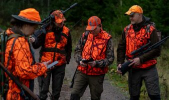 Metsästyksenjohtaja jakaa käskyjä oranssiin vaatetukseen pukeutuneille metsästäjille.